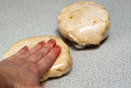 Pressing pie crust ingredients in plastic wrap into flat disks.