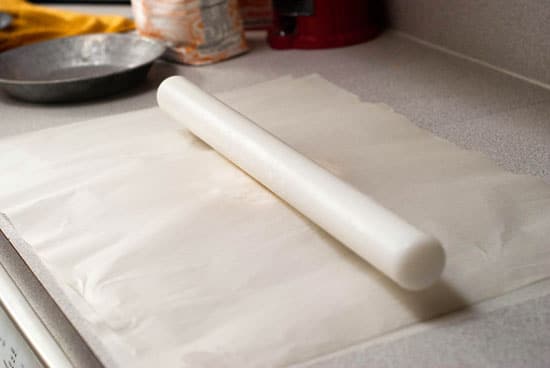 Parchment paper with delicious pie dough in the middle with a rolling pin on top.