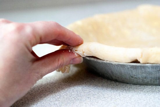 Tucking edges of pie crust dough onto a pie dish.