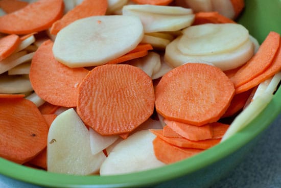 Sliced sweet potatoes and russet potatoes in a large green bowl.