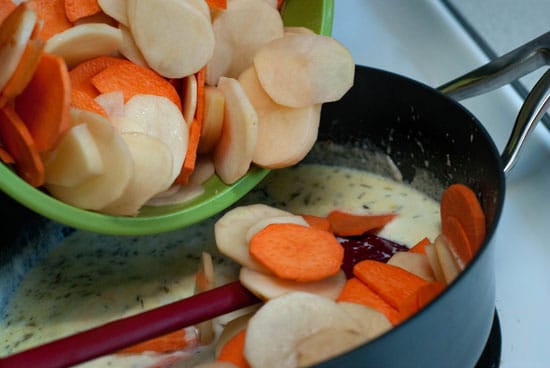 Pouring sliced potatoes into ingredient mixture in a large skillet.