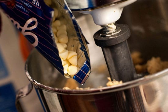 Pouring white chocolate chips into an electric mixer.