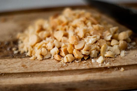 Chopped macadamia nuts on a wooden cutting board.