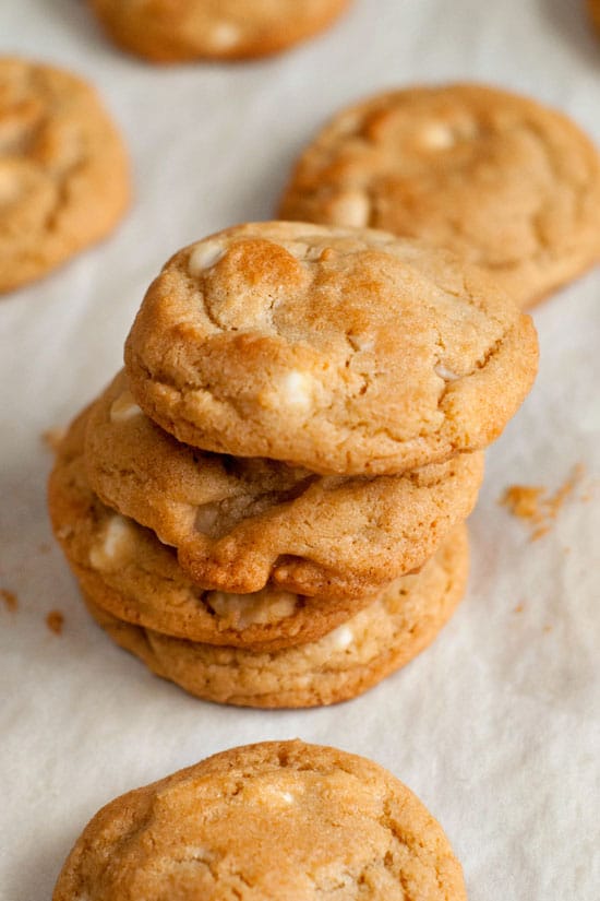 Stacked White Chocolate Macadamia Nut Cookies on parchment papers.