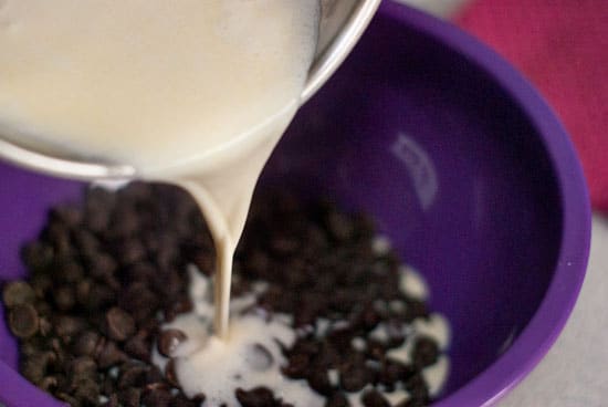 Fresh cream and butter poured of semi sweet chocolate chips in a large purple bowl.