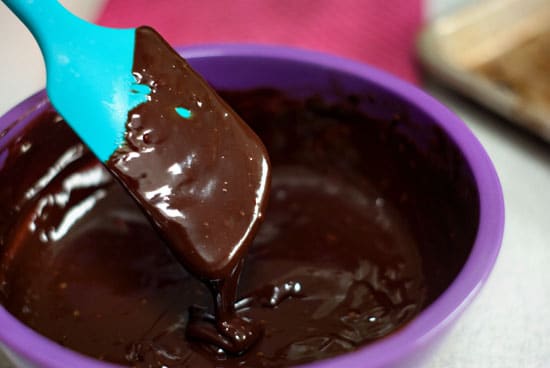 Smooth and creamy chocolate ganache in a large purple bowl with a blue spatula.