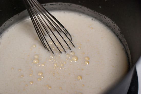 Whisking egg mixture together in a large black saucepan.