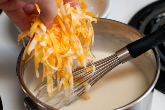 Mixing shredded colby jack cheese in to this easy Cheese Sauce in a silver sauce pan.