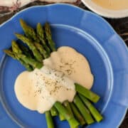 Asparagus drizzled with this Basic Cheese Sauce on a large blue plate.