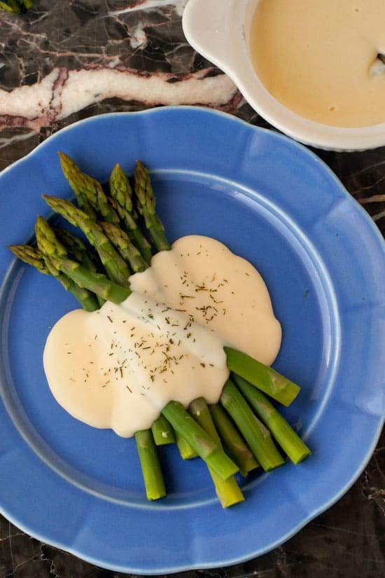 Basic Cheese Sauce on fresh asparagus on a blue serving plate.