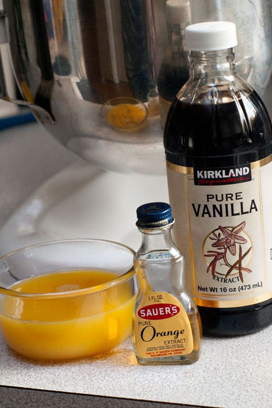 Orange juice, orange extract and pure vanilla extract next to a silver mixing bowl.