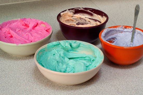 Green, pink, purple and peach assortment of cookie icing in small bowls.