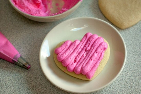 Fresh pink icing on a delicious and soft sugar cookie on a small plate.