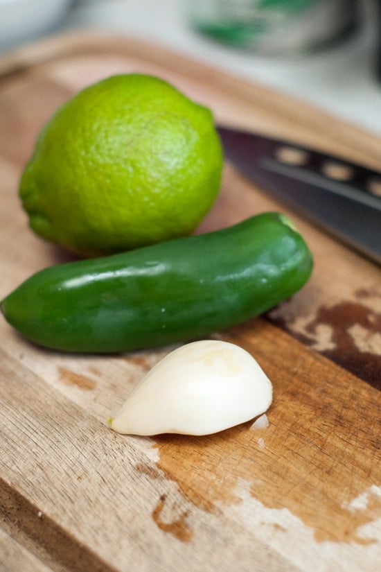 Lime, jalapeno and a garlic clove on a wooden cutting board.