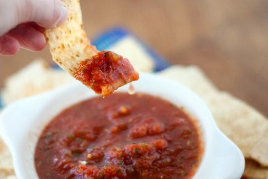 Scooping simple Salsa with a tortilla chips out of a small white bowl.