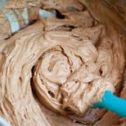 Mixing fluffy chocolate frosting in a mixing bowl with a blue spatula.