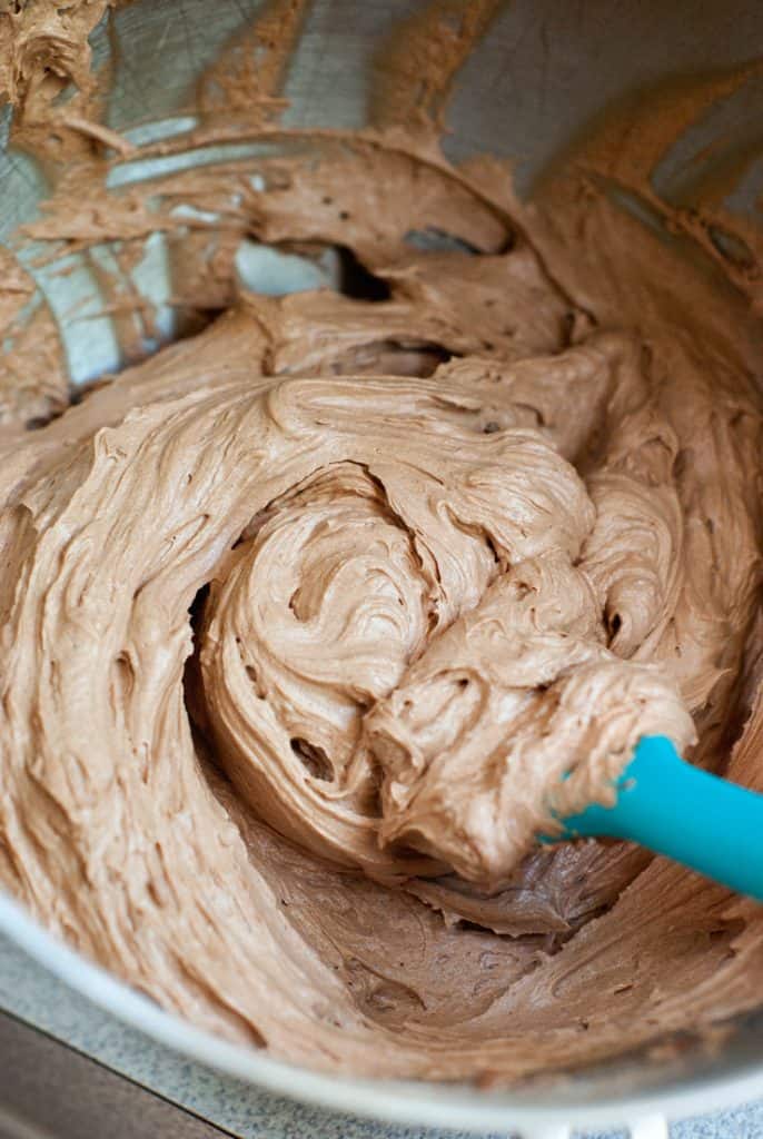 Mixing simple Chocolate Frosting in a mixing bowl with a blue spatula.