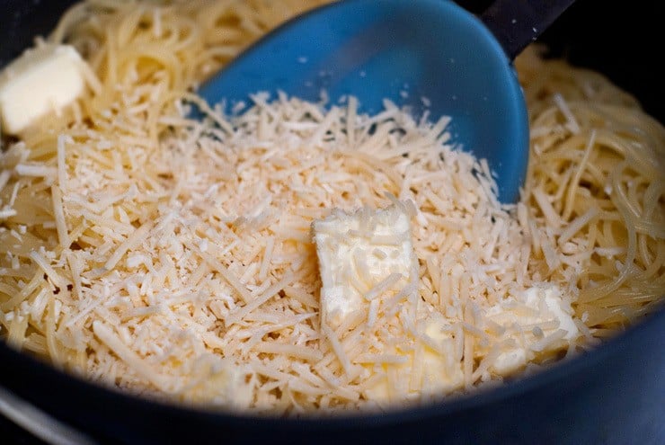 Cooked pasta, butter and shredded Parmesan cheese in a black skillet.