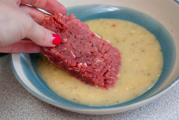 Dipping shredded beef into mixture in a blue and white bowl.