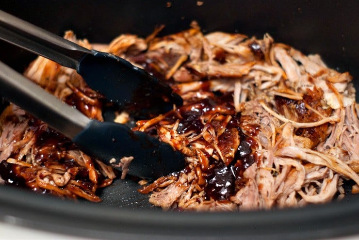 Crock Pot Blackberry BBQ Pulled Pork being grabbed with a pair of tongs.