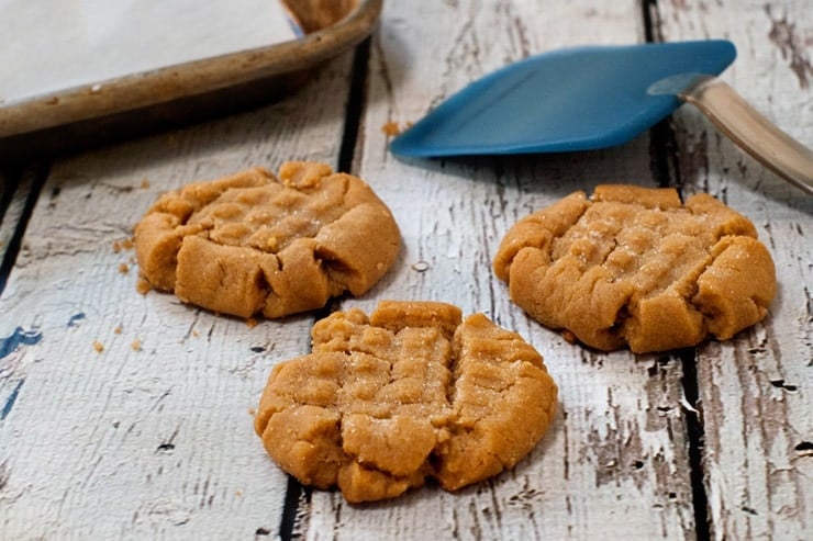 Three of the BEST Peanut Butter Cookies on a wooden table next to a blue spatula.