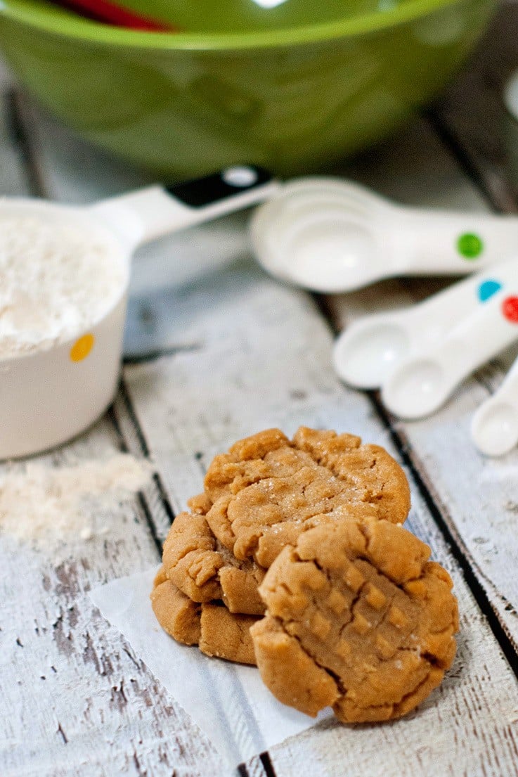 Three delicious Peanut Butter Cookies next to measuring spoons on a wooden table.