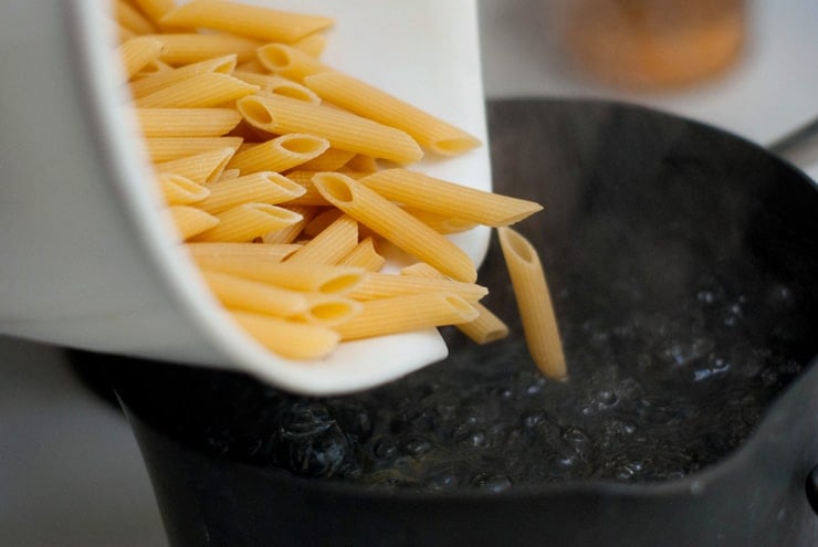 Pouring cooked Penne Pasta into a skillet.