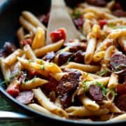 Easy Penne With Smoked Sausage and Caramelized Onions in a skillet with a wooden spoon.