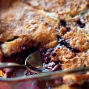 Scooping out Boysenberry Cobbler out of a cake pan with a silver spoon.