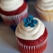 Two simple Red Velvet Cupcakes with delicious cream cheese frosting and a blue flower on top.