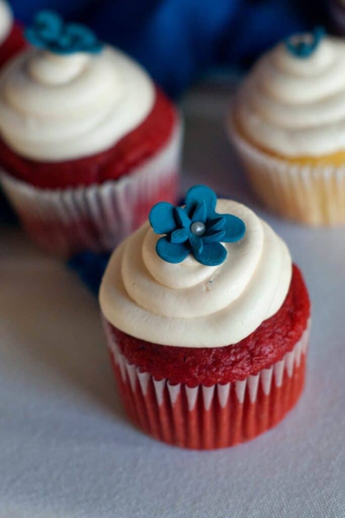 Two Easy Red Velvet Cupcakes with cream cheese frosting and a blue decorative flower on top.