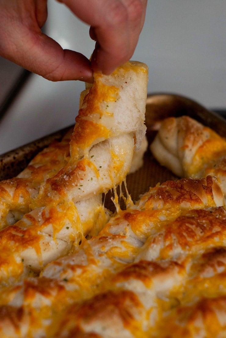 Pulling Cheesy Garlic Breadsticks apart in a baking sheet.