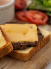 Texas Toast Griddle Burger patty on buttered bread on a wooden board.