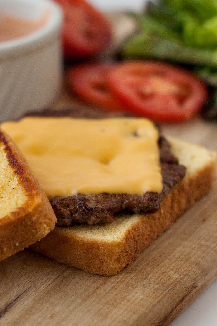 Burger patty with yellow cheese on toasted buttered bread on a wooden board.