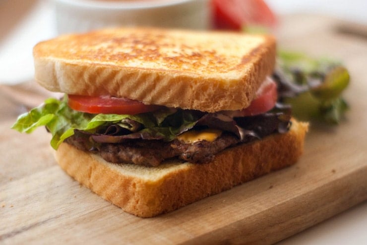 Easy Texas Toast Griddle Burger with tomatoes and lettuce on a wooden board.