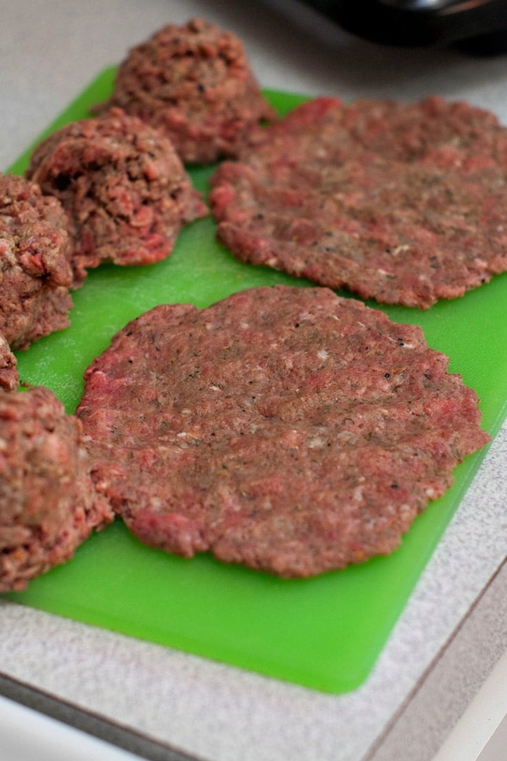 Seasoned Burger Patties on a green cutting board.