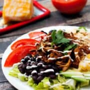 Simple Slow Cooker BBQ Chicken Taco Salad with cheese, black beans and tomatoes on a white plate.