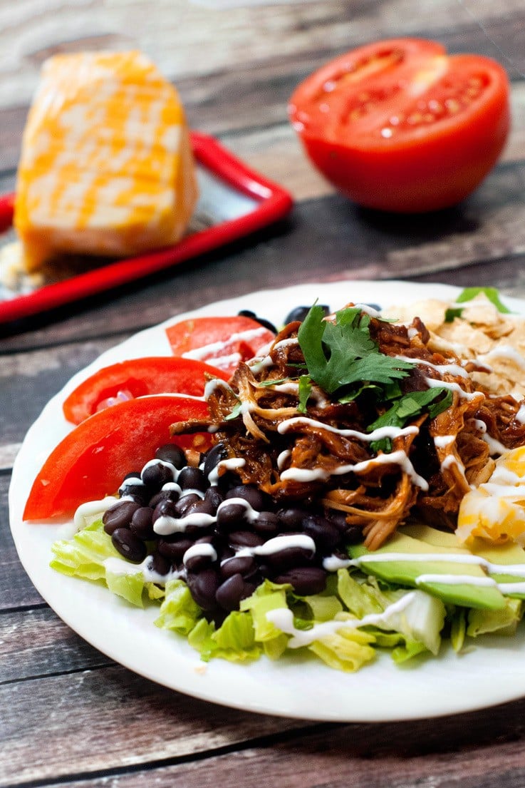 Easy crock pot BBQ Chicken Taco Salad with fresh tomatoes and black beans on a white serving plate.