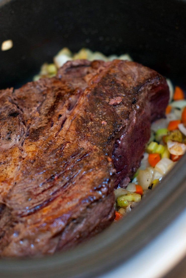 Easy Slow Cooker Pot Roast on a bed of celery, onions and carrots in a slow cooker.