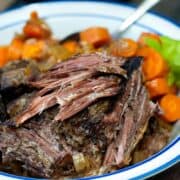 Classic Slow Cooker Pot Roast with carrots, onions and celery on a blue and white plate.
