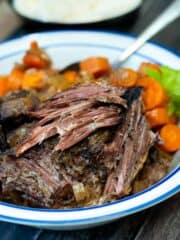 Classic Slow Cooker Pot Roast with carrots, onions and celery on a blue and white plate.