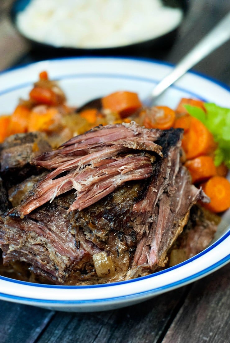 Shredded Crock Pot Pot Roast with healthy veggies on a white and blue plate on a wooden table.