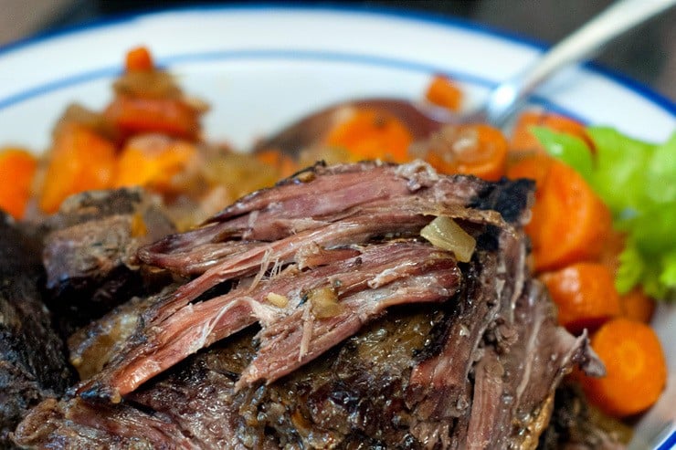 Classic Slow Cooker Pot Roast recipe with carrots on a blue and white plate with a silver spoon.