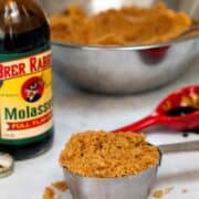 Silver measuring cup of homemade brown sugar next to a glass bottle of molasses.