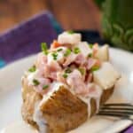 Baked Potato with ham, turkey, cheese and diced green onions on a white serving plate.