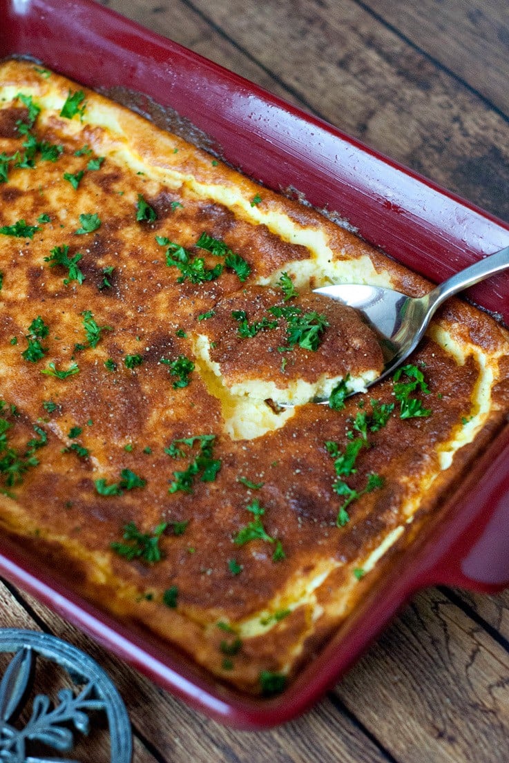 Scooping delicious Cheddar Garlic Corn Bread with a silver spoon out of a red casserole dish.