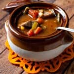 Delicious Slow Cooker Vegetable Beef Soup in a smalll white and brown bowl on a wooden table.