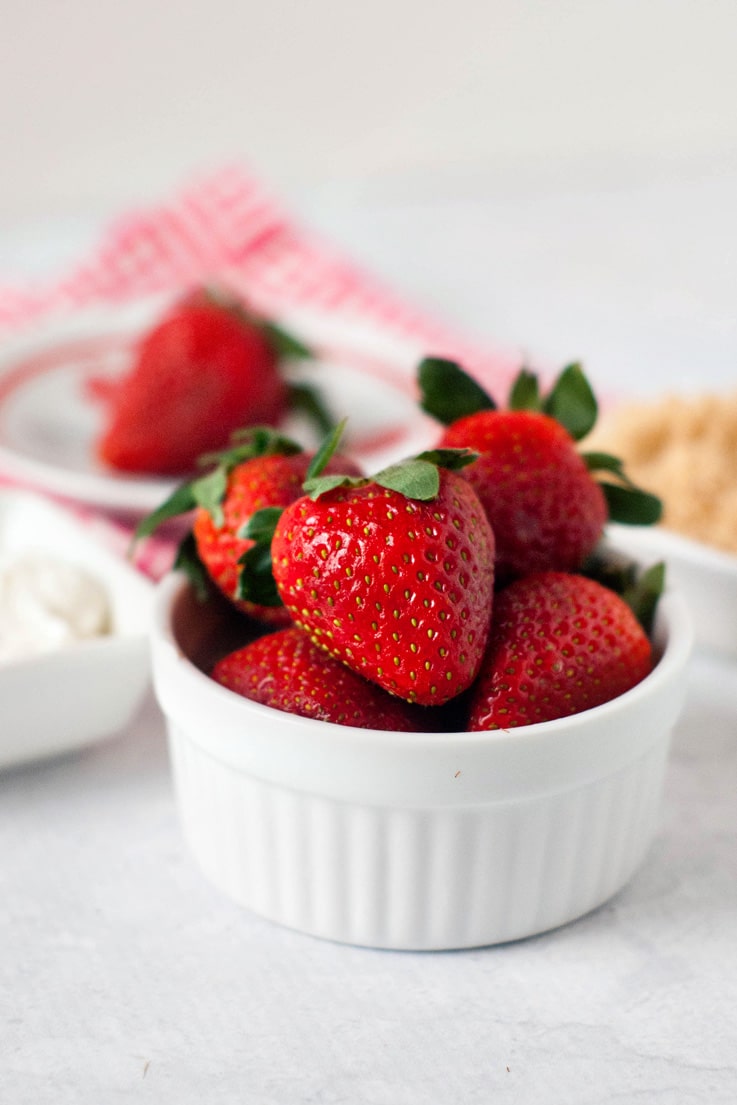 A bowl of strawberries getting ready to dip in sour cream and brown sugar