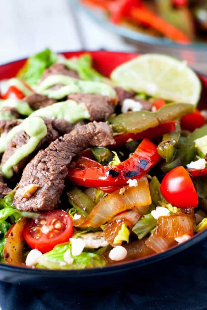 Skillet Steak Fajita Salad in red bowl with slice of lime