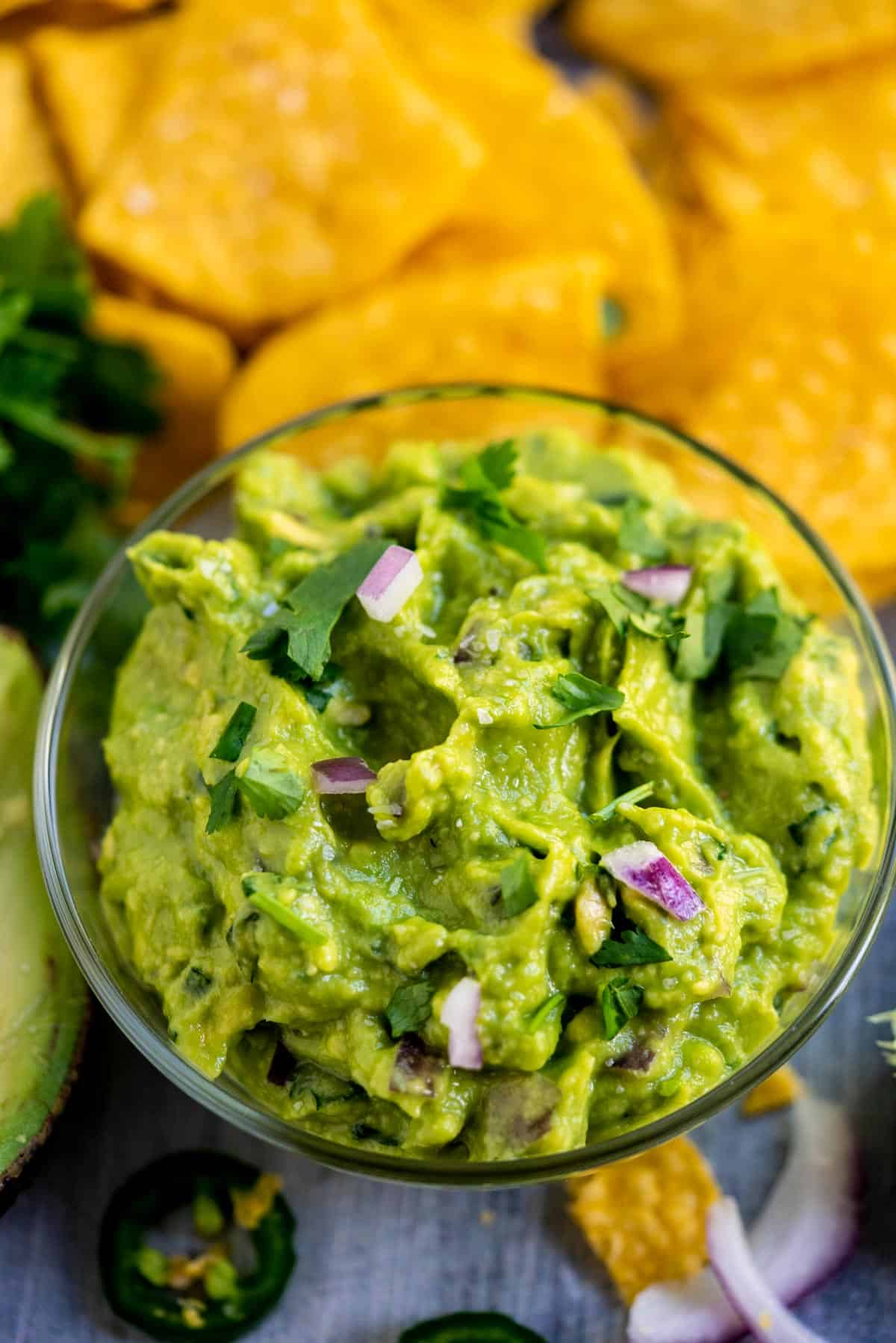 Guacamole with red onion and chip in a glass bowl